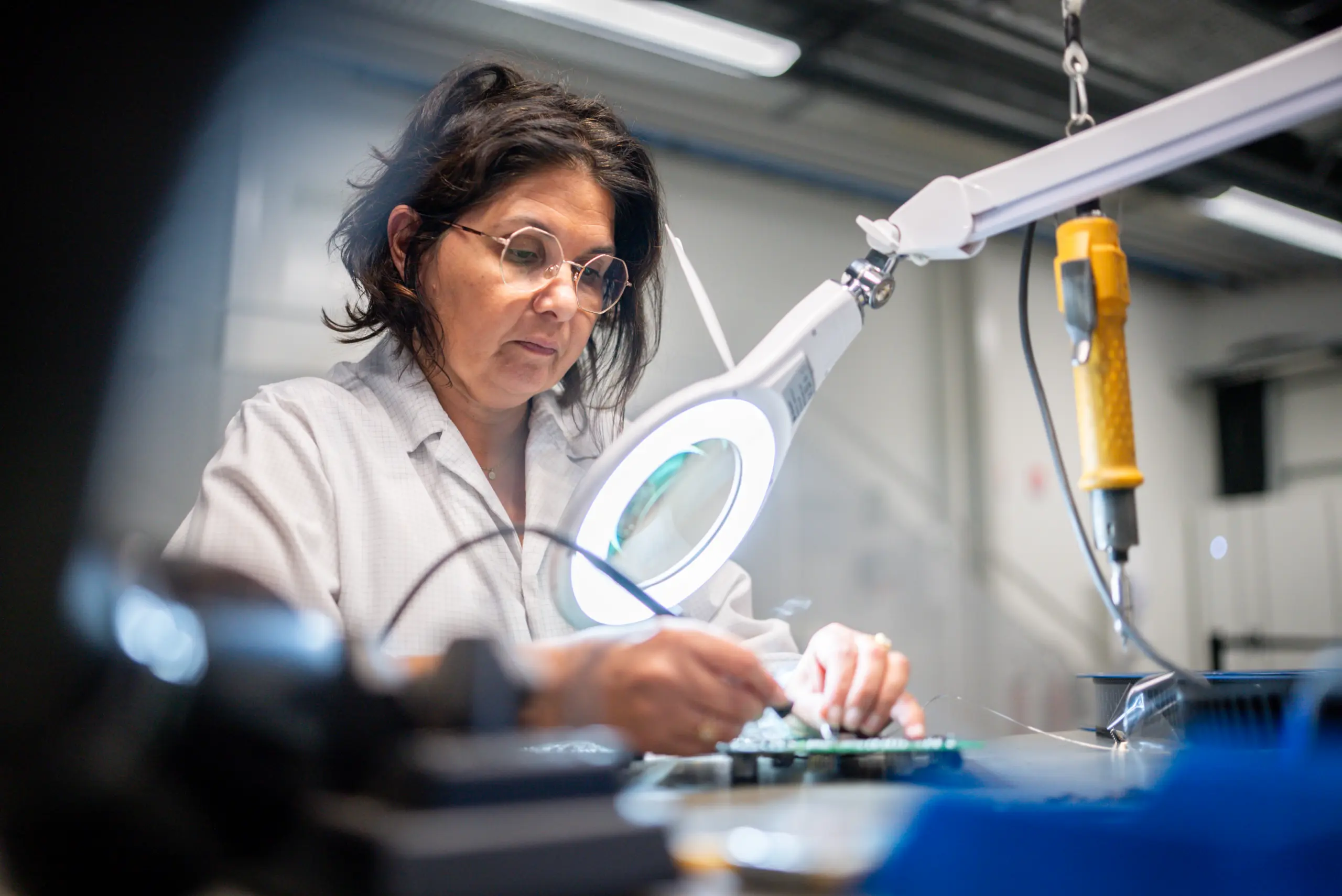 Technicienne réalisant un contrôle qualité minutieux sur une carte électronique pour garantir la fiabilité des lecteurs LiNEGUARD